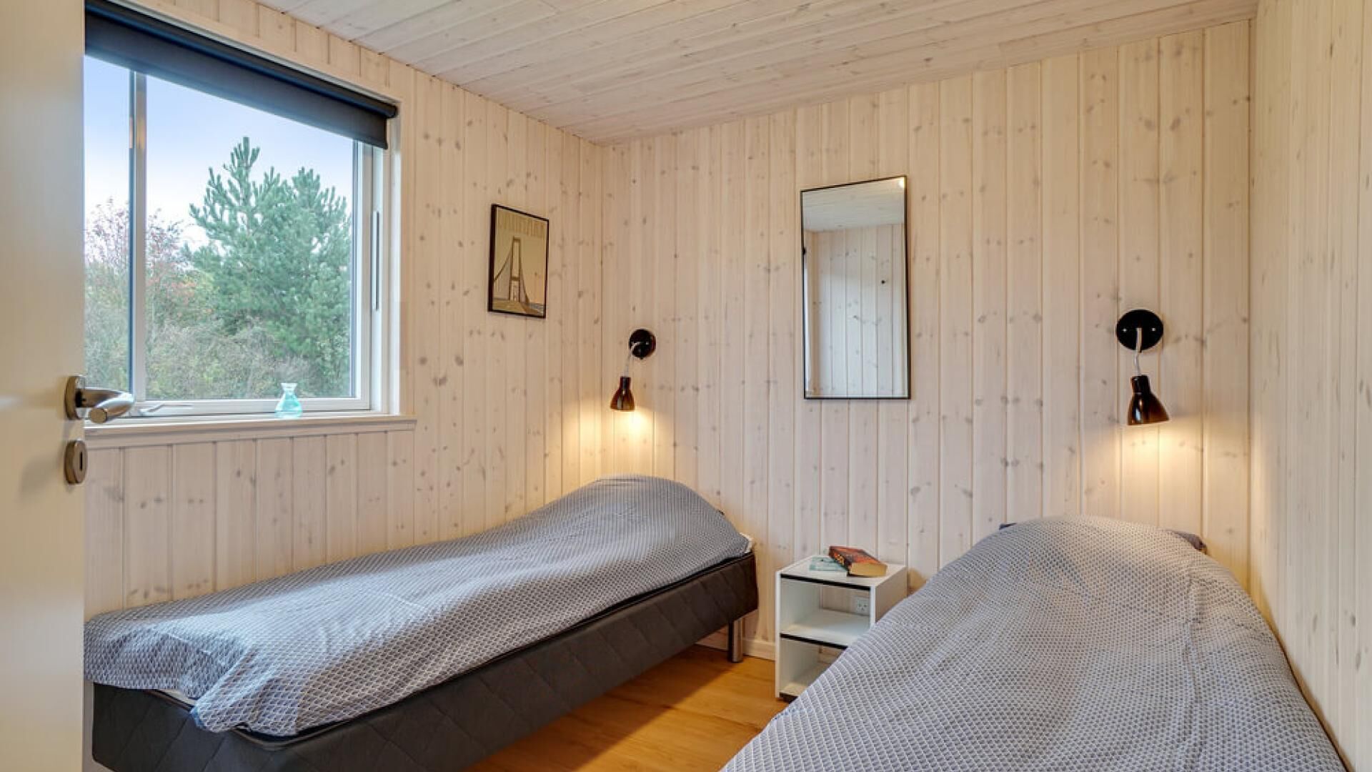 Une chambre avec deux lits simples, une fenêtre donnant sur la verdure et une petite table de chevet avec une lampe.
