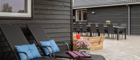 An outdoor seating area with two lounge chairs, a wooden table, and a flower arrangement.