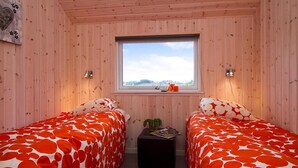 Ein Zimmer mit zwei Betten, einem Fenster, einem kleinen Tisch mit einer Pflanze und einer Wandleuchte.