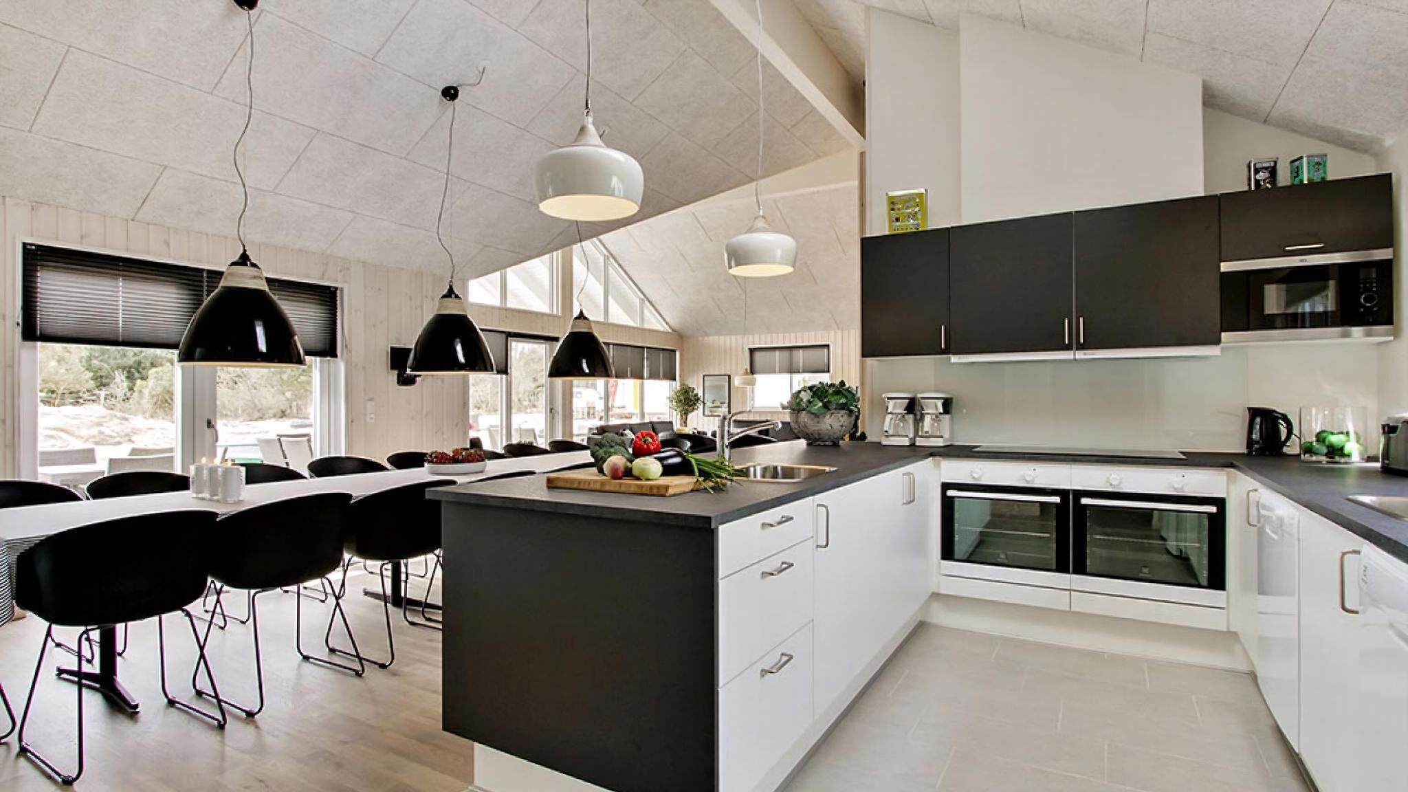A modern kitchen with a large island, black pendant lights, and a dining area with chairs.