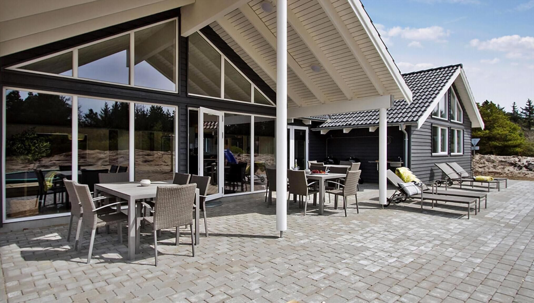 A covered outdoor patio with tables and chairs, a pool, and a building with large windows.