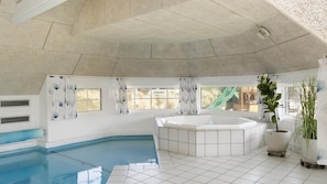 Ein großes Hallenbad mit Whirlpool, umgeben von Fenstern mit Vorhängen und Blick auf einen Spielplatz.