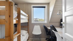Ein kleines Zimmer mit Etagenbetten, einem Schreibtisch, zwei Stühlen und einem Fenster mit Blick auf ein Haus und einen Hügel.