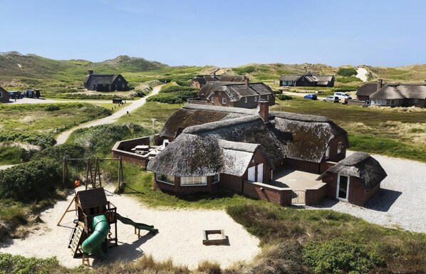 A rural setting with thatched-roof cottages, a sandy play area, and a gravel path. - VillaVilla 675 - Søndervig, Vestjylland (Ringkøbing)