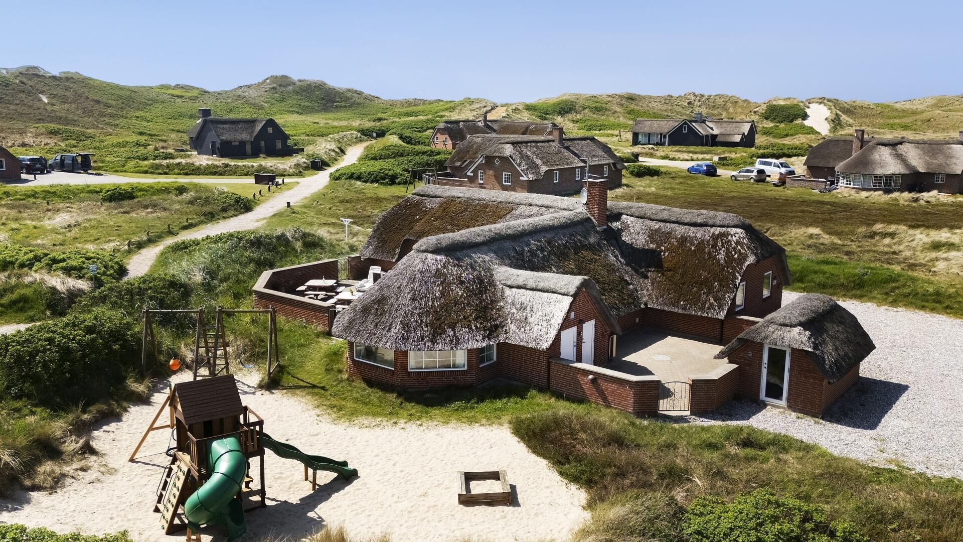 A traditional thatched-roof building with a sandy path leading to it, surrounded by similar structures in a rural setting.