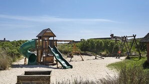 Eine Holzspielanlage mit Rutsche und Schaukeln am Sandstrand.