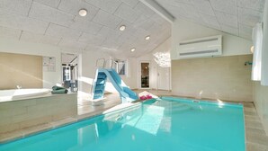 Une piscine intérieure avec un toboggan bleu, un jacuzzi et un plafond doté d’un éclairage encastré.
