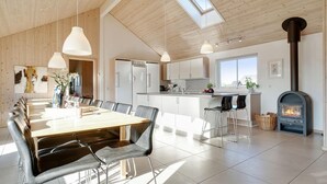 Une cuisine moderne dotée d’un îlot central, d’un coin repas avec une longue table et des chaises, et d’un poêle à bois.