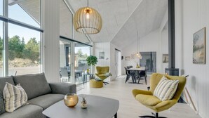 Un vaste espace de vie comprenant un canapé moderne, un fauteuil jaune et une table à manger.