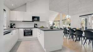 Une cuisine moderne avec des meubles blancs, un four encastré et un coin repas comprenant des chaises noires et une table en bois.