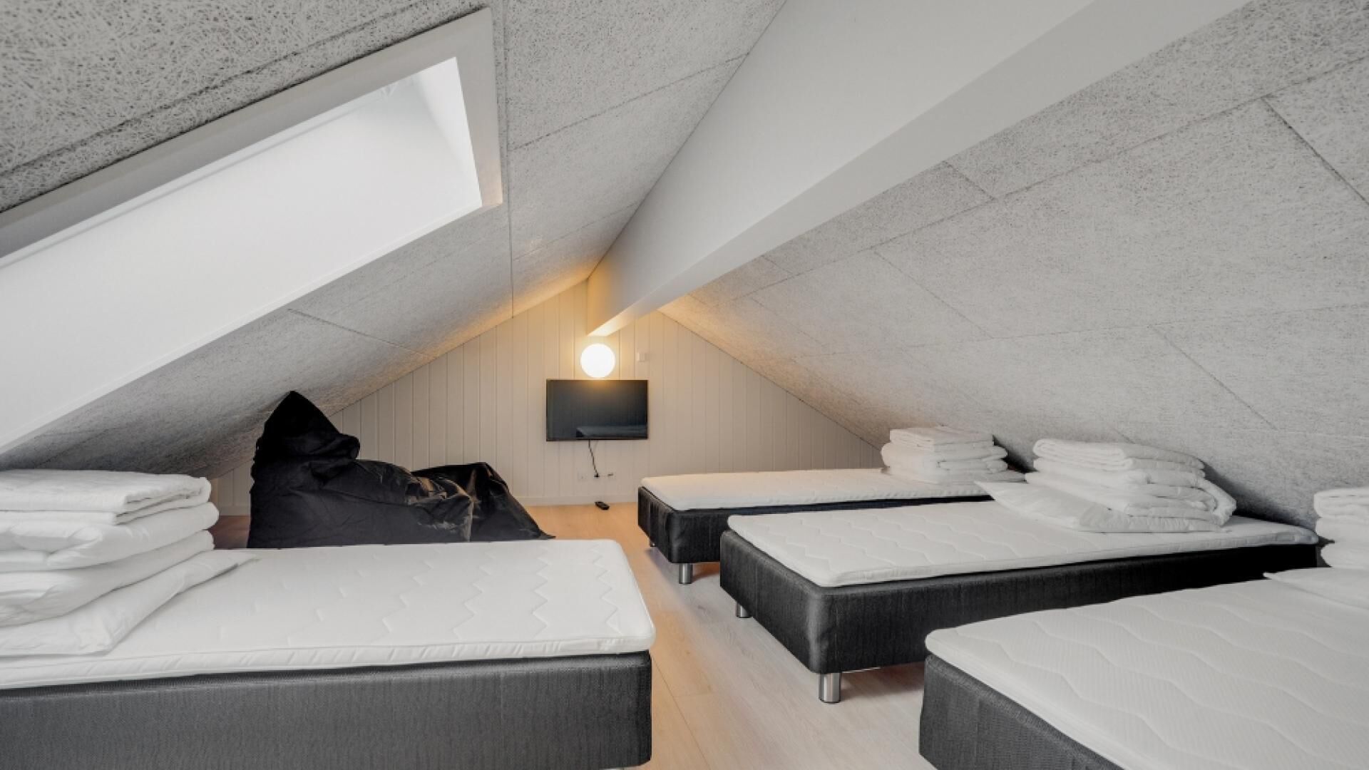 Un dormitorio moderno en el ático con tres camas, un sillón informal negro y un televisor montado en la pared.
