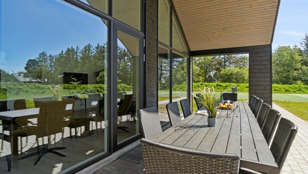 Un espace extérieur abrité, aménagé pour les repas, avec une grande table et des chaises, de grandes fenêtres et une vue sur un paysage verdoyant.