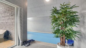 Une salle de bain moderne avec une douche à parois de verre, une grande plante en pot et une piscine visible à travers le verre.