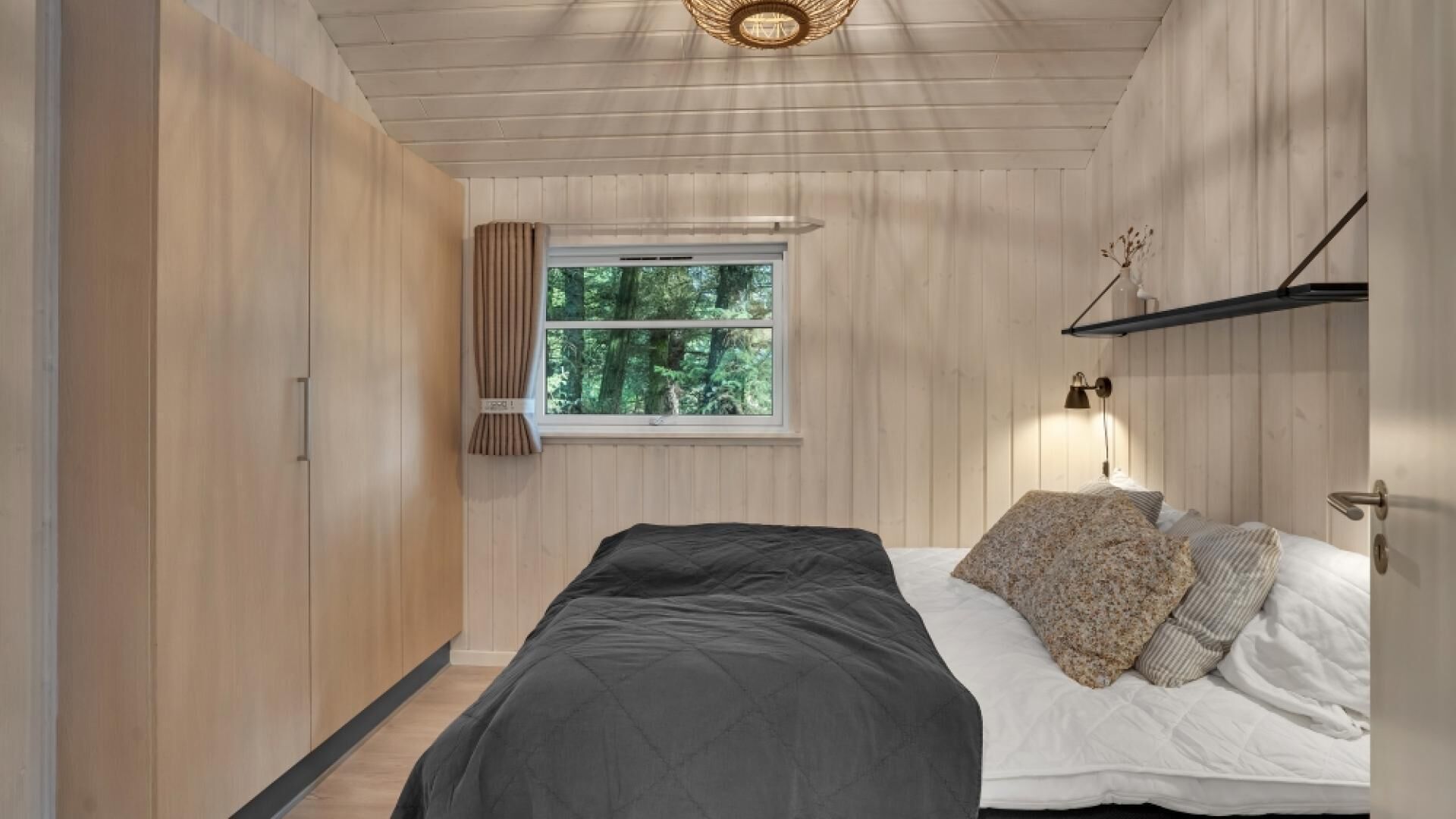 Une chambre à coucher avec un lit, une fenêtre avec des rideaux, une lampe de chevet et une étagère avec des objets décoratifs.