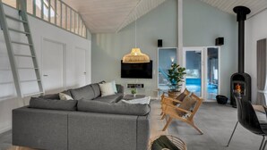 Een moderne woonkamer met een grijze bank, een houten salontafel, een aan de muur bevestigde televisie en een open haard.