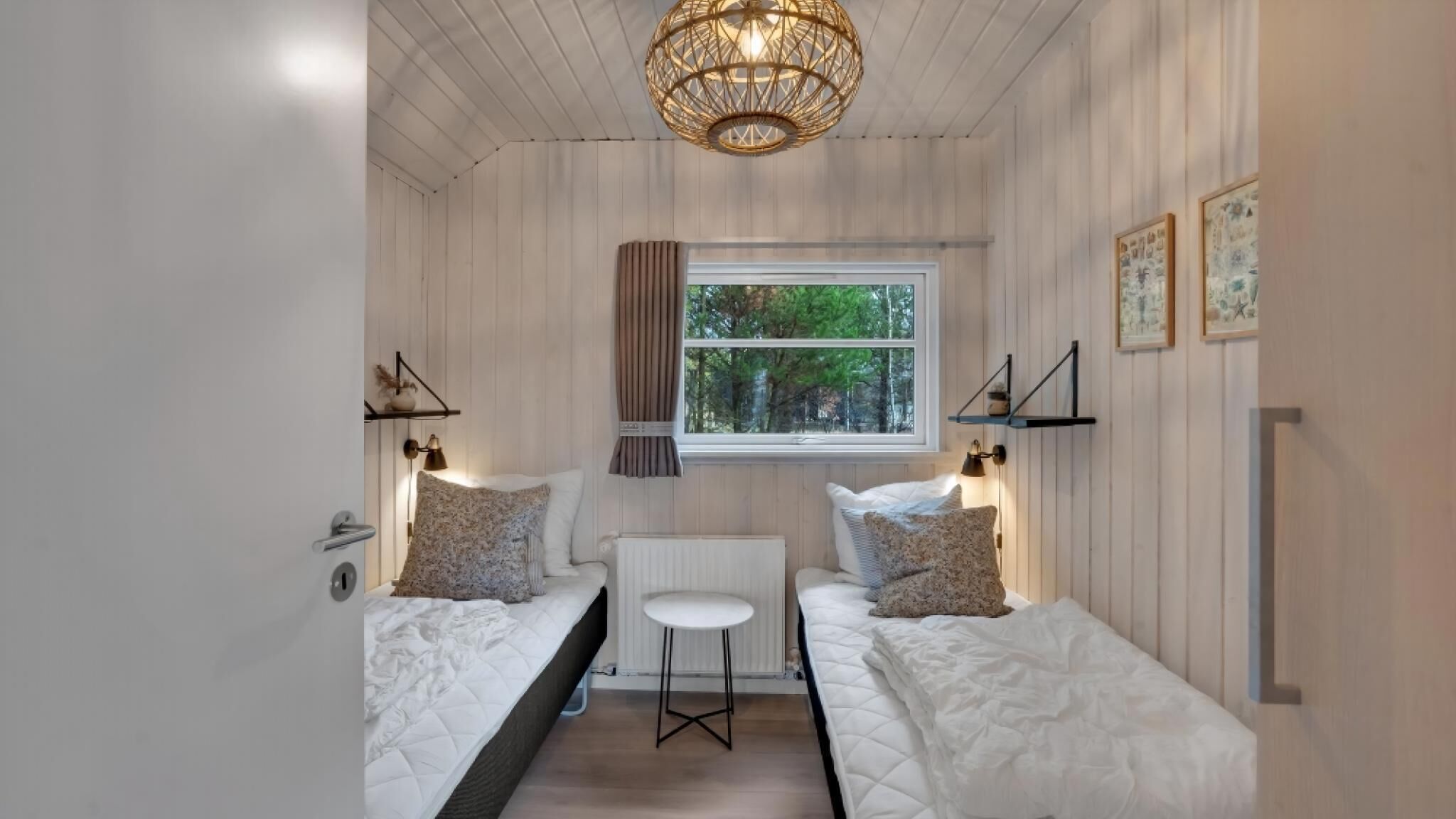 Une petite pièce agréable et chaleureuse, avec deux lits, une fenêtre donnant sur les arbres, une table et un luminaire suspendu.