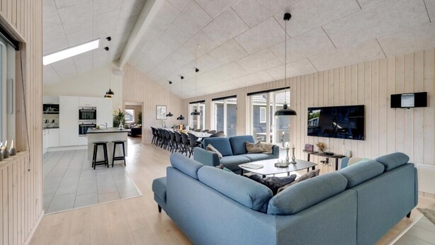 En rummelig opholdsstue med en stor blå sofa, et spisebord og et køkken i baggrunden.