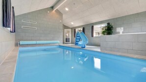 En indendørs swimmingpool med blå rutsjebane, grå flisevægge og indbyggede loftslamper.