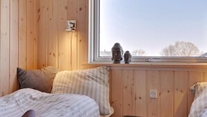 Ett mysigt rum med träväggar, en säng med randigt sänglinne, ett fönster med utsikt över träd och en liten statyett på fönsterbrädan.