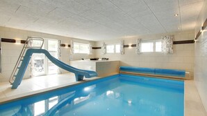 Una piscina interior amb tobogan blau, una taquilla d'admissions i una finestra amb cortines.