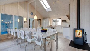 Een moderne keuken met een centraal eiland, witte stoelen, een eettafel en een houtkachel.