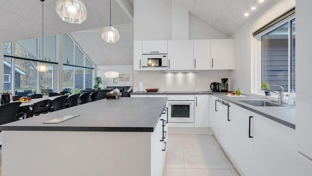 A modern kitchen with a large island, white cabinetry, and a large window providing natural light. - VillaVilla 513 - Marielyst, Lolland/Falster/møn (Væggerløse)