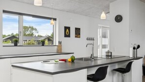 A modern kitchen with a large island, pendant lights, and a view of houses outside. - VillaVilla 642 - Marielyst, Lolland/Falster/møn (Væggerløse)