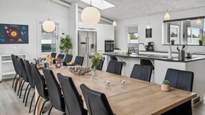 A modern kitchen with a central island, a dining area with a wooden table and black chairs, and a large window providing natural light. - VillaVilla 642 - Marielyst, Lolland/Falster/møn (Væggerløse)