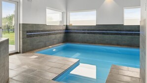 A modern indoor swimming pool with a clear blue water, grey tiled walls, and a glass door leading outside. - VillaVilla 642 - Marielyst, Lolland/Falster/møn (Væggerløse)