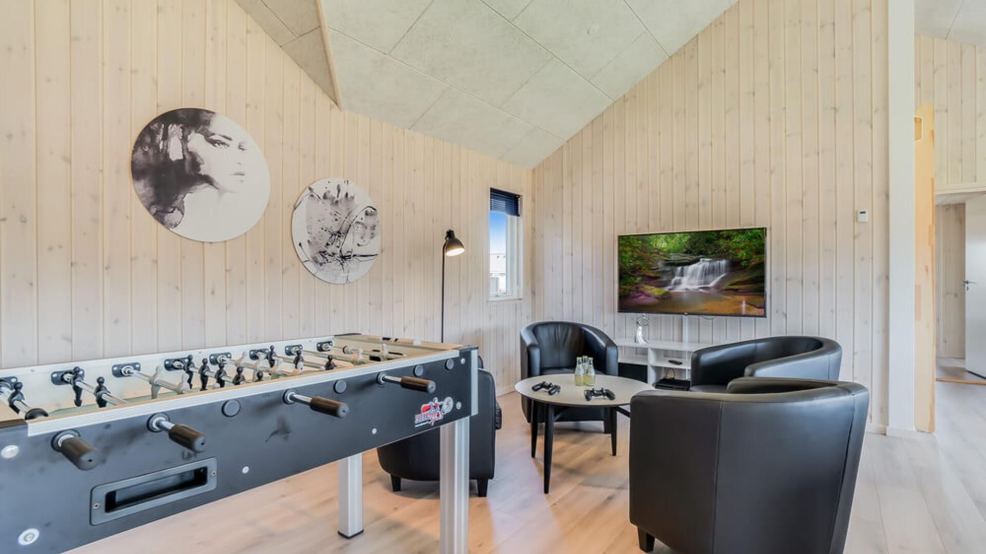 A room with a foosball table, a TV, and a seating area with two chairs.
