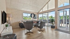 Ett rymligt vardagsrum med ett träpanelat tak, en soffgrupp, ett soffbord och en tv som är monterad på väggen.