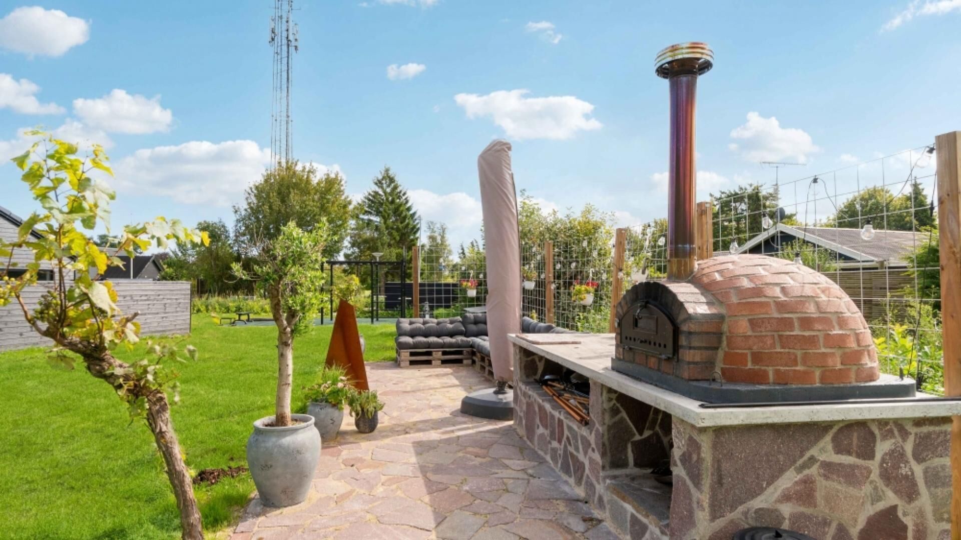 A stone patio with a brick oven, outdoor seating, and a tall chimney.