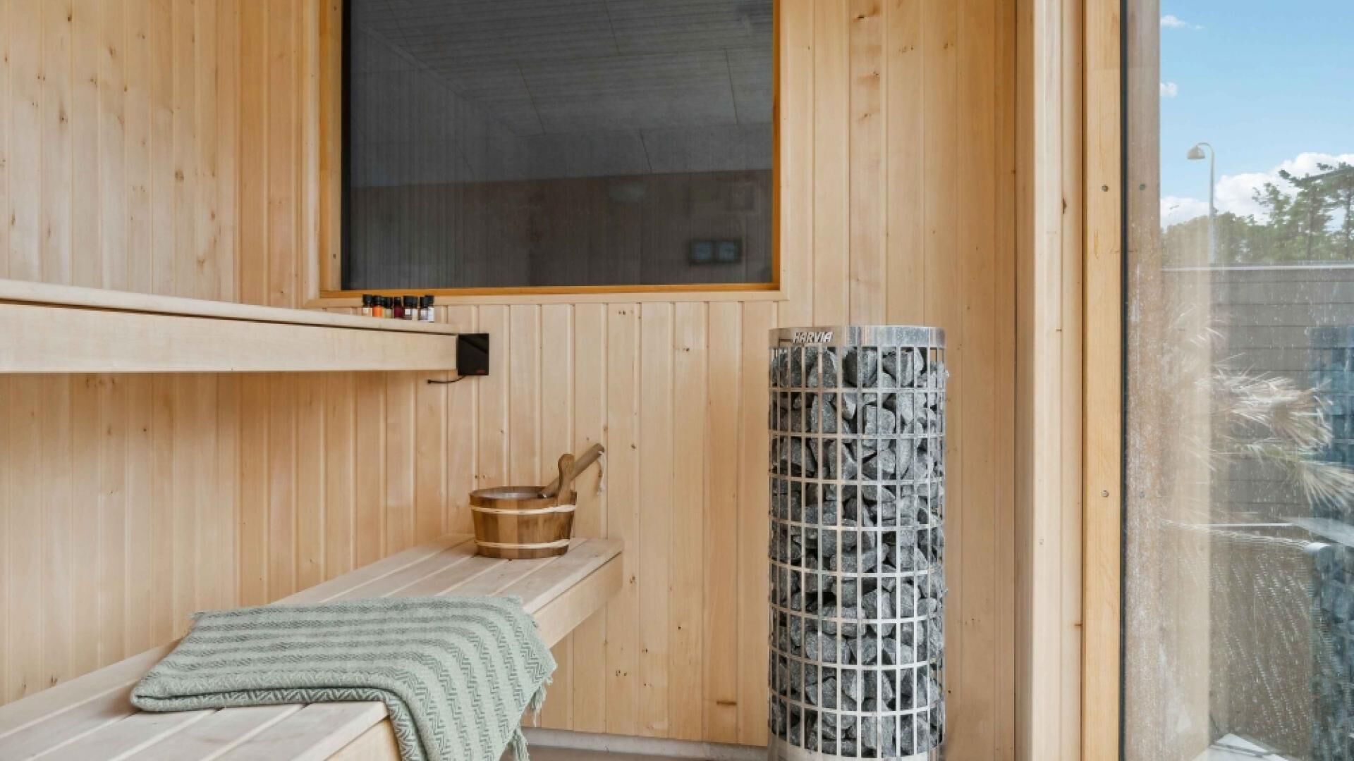 A wooden sauna room with a bench, a stone heater, and a window.