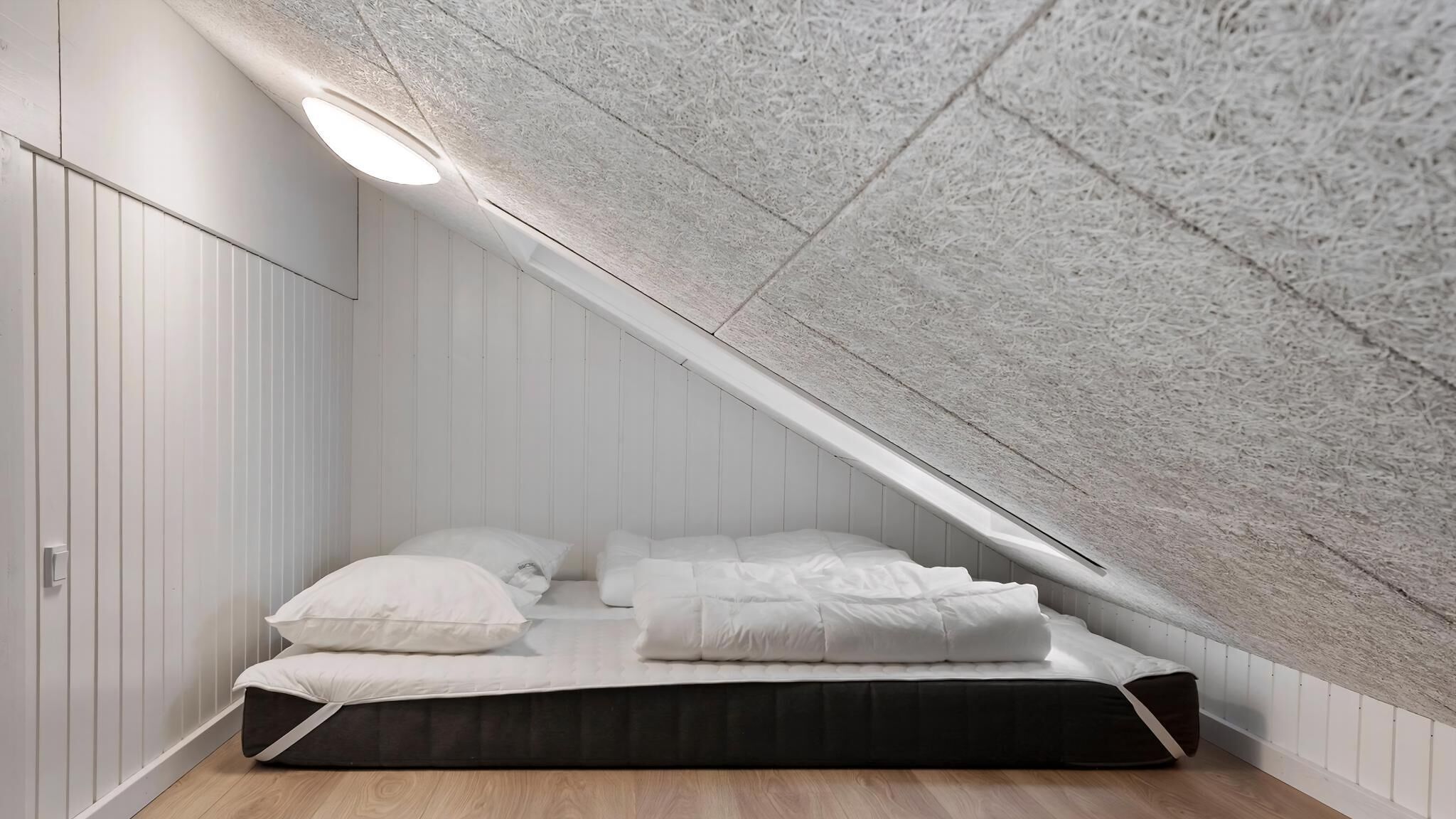 A small, sloped ceiling room with a bed, white walls, and a wooden floor.