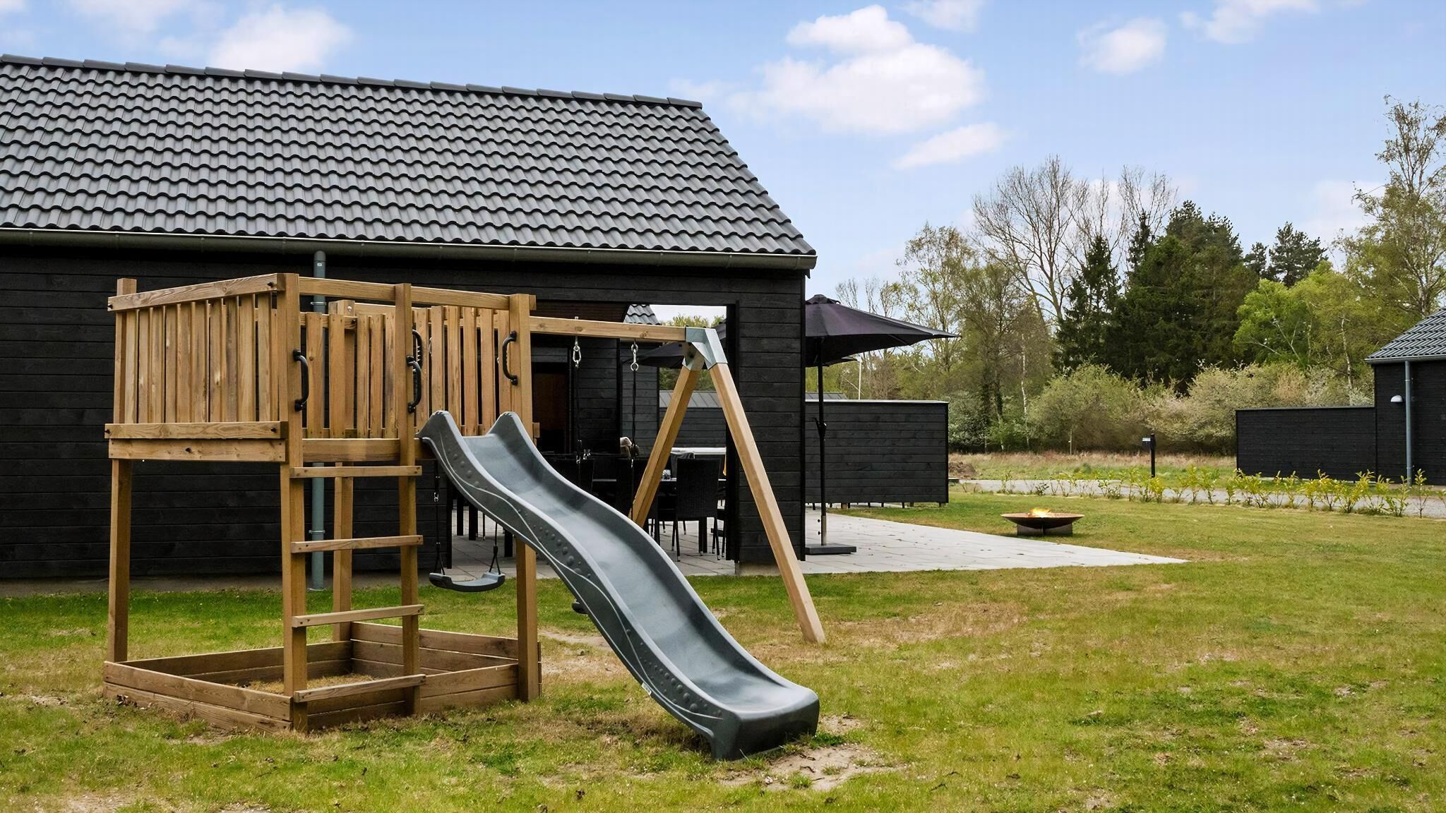 Ein Spielplatz mit Rutsche und Klettergerüst, ein Grillplatz und ein Gebäude mit einem Ziegeldach.