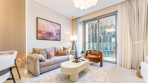 Un salon moderne avec un canapé, une table basse et un fauteuil. Une grande fenêtre, ornée de rideaux, laisse entrer la lumière, et un tableau est accroché au mur.