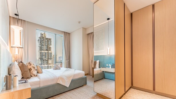Une chambre d’hôtel moderne avec un grand lit, une table de chevet, un miroir et une vue sur un immeuble en construction.