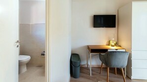 A modern, minimalistic room with a wooden desk, a television, and a grey chair. - Near the lake and the center (FLORIDA ASCONA Room 09) (Ascona)