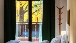 Une chambre d’hôtel avec un lit, une vue sur un balcon orné d’un arbre et un porte-manteau.