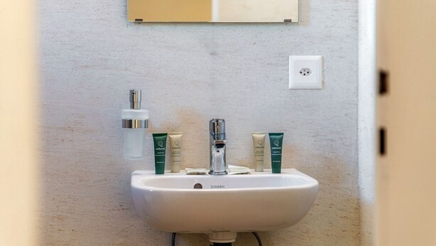 Un lavabo dans une salle de bain, avec un miroir au-dessus, un robinet et trois flacons de lotion.