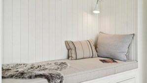 A corner of a room with a white padded bench, two pillows, a fur throw, and a wall-mounted light fixture. - VillaVilla 620 - Marielyst, Lolland/Falster/møn (Væggerløse)