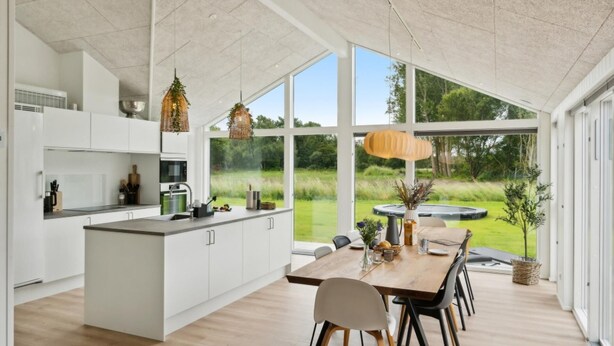 A modern kitchen with a large island, white cabinetry, and a dining area with a wooden table and chairs. - VillaVilla 620 - Marielyst, Lolland/Falster/møn (Væggerløse)