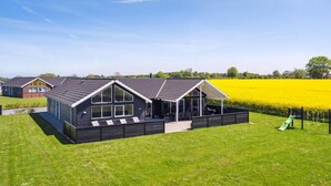 A modern house with a large patio, a covered outdoor area, and a field of yellow flowers in the background. - VillaVilla 345 - Skåstrup Strand, Fyn og øer (Bogense)
