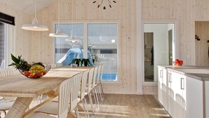 A modern kitchen with a wooden interior, a dining area with a wooden table and chairs, and a view of a blue outdoor area. - VillaVilla 345 - Skåstrup Strand, Fyn og øer (Bogense)