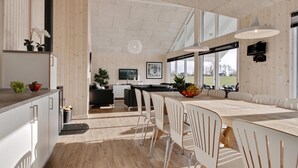 A modern kitchen with a dining area, featuring a large island, white cabinetry, and a view of the outdoors. - VillaVilla 345 - Skåstrup Strand, Fyn og øer (Bogense)