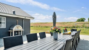 Un patio al aire libre con una parrilla, mesa de comedor, sillas y un arreglo floral.