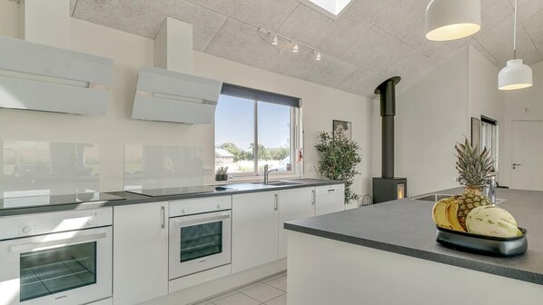 A modern kitchen with white cabinetry, a built-in oven, a stove, and a large window.