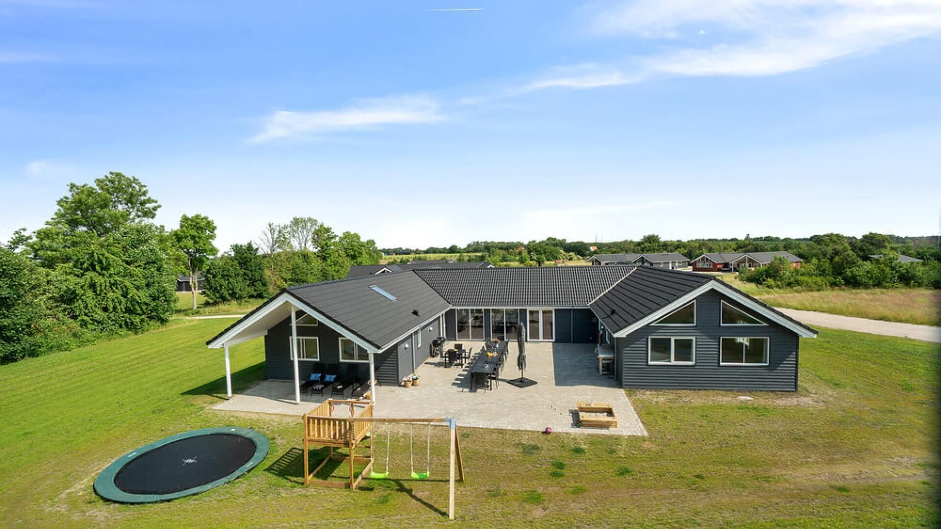Een modern huis met een ruim terras, een schommel en een trampoline.