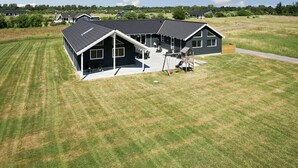 A large, two-story house with a sloped roof, a covered patio, and a fenced yard. - VillaVilla 343 - Marielyst, Lolland/Falster/møn (Væggerløse)