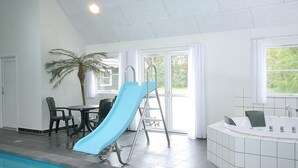 Un espace piscine avec un toboggan, une table entourée de chaises, un palmier et une baignoire.